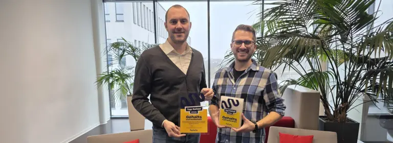 MID GmbH | kununu Top Rated-Siegel Gehaltszufriedenheit 2025, zwei Mitarbeitende zeigen das Auszeichnungsschild im modernen Büro mit Pflanzen; Header-Bild zur News über besondere Arbeitgeberattraktivität.