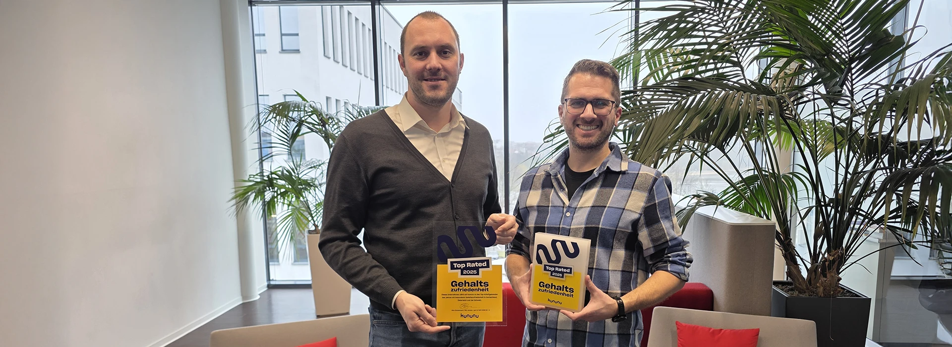 MID GmbH | kununu Top Rated seal for salary satisfaction 2025 — two employees holding the award plaque in a modern office with plants; header image for a news article about MID’s outstanding employer appeal.