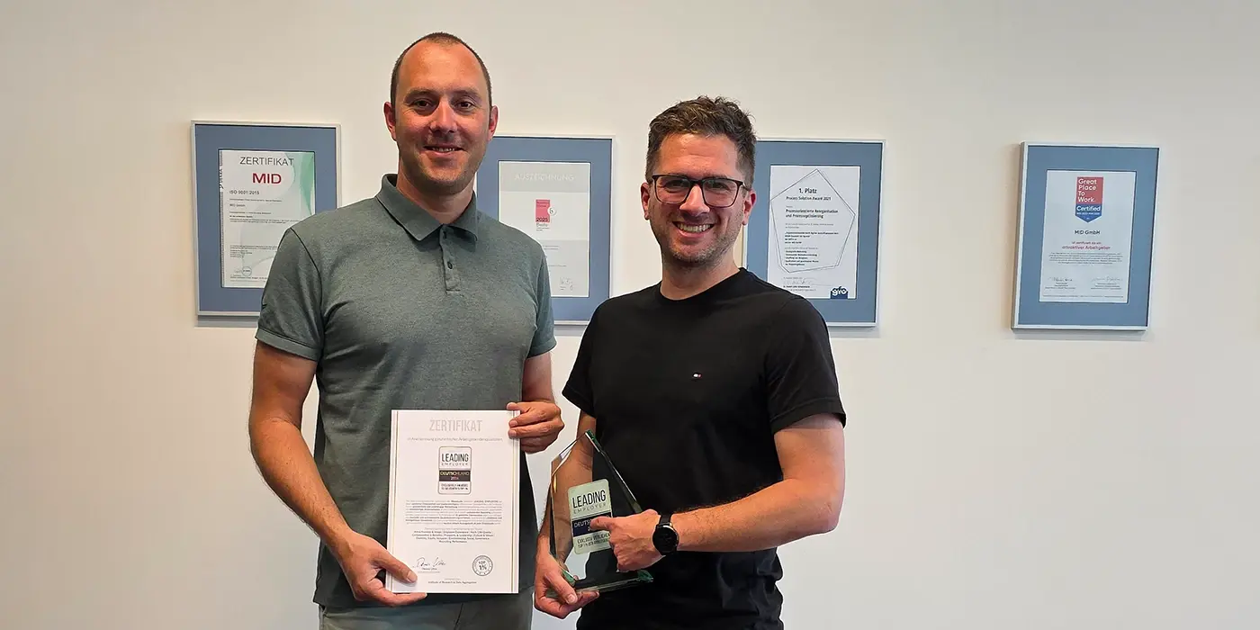 MID-GmbH-News-Leading Employer-Auszeichnung-2026 MID GmbH | Leading Employer 2026 – Stefan Klein und Patrick Düber präsentieren Urkunde und Trophäe vor einer Wand mit gerahmten Urkunden; Header-Bild zur News über die Auszeichnung als attraktiver Arbeitgeber.