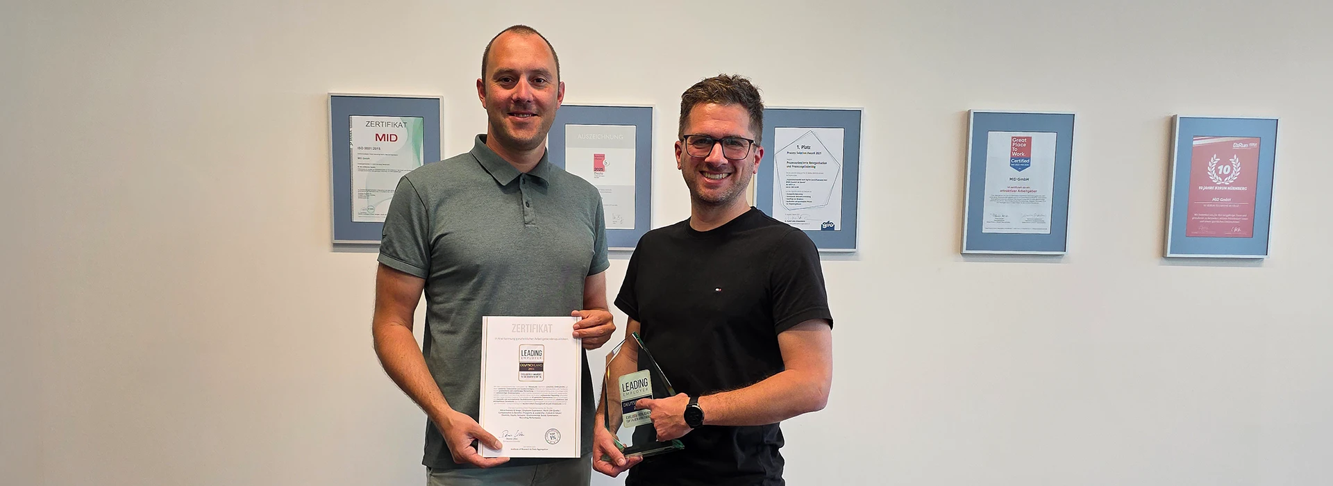 MID GmbH | Leading Employer 2026 – Stefan Klein und Patrick Düber präsentieren Urkunde und Trophäe vor einer Wand mit gerahmten Urkunden; Header-Bild zur News über die Auszeichnung als attraktiver Arbeitgeber.